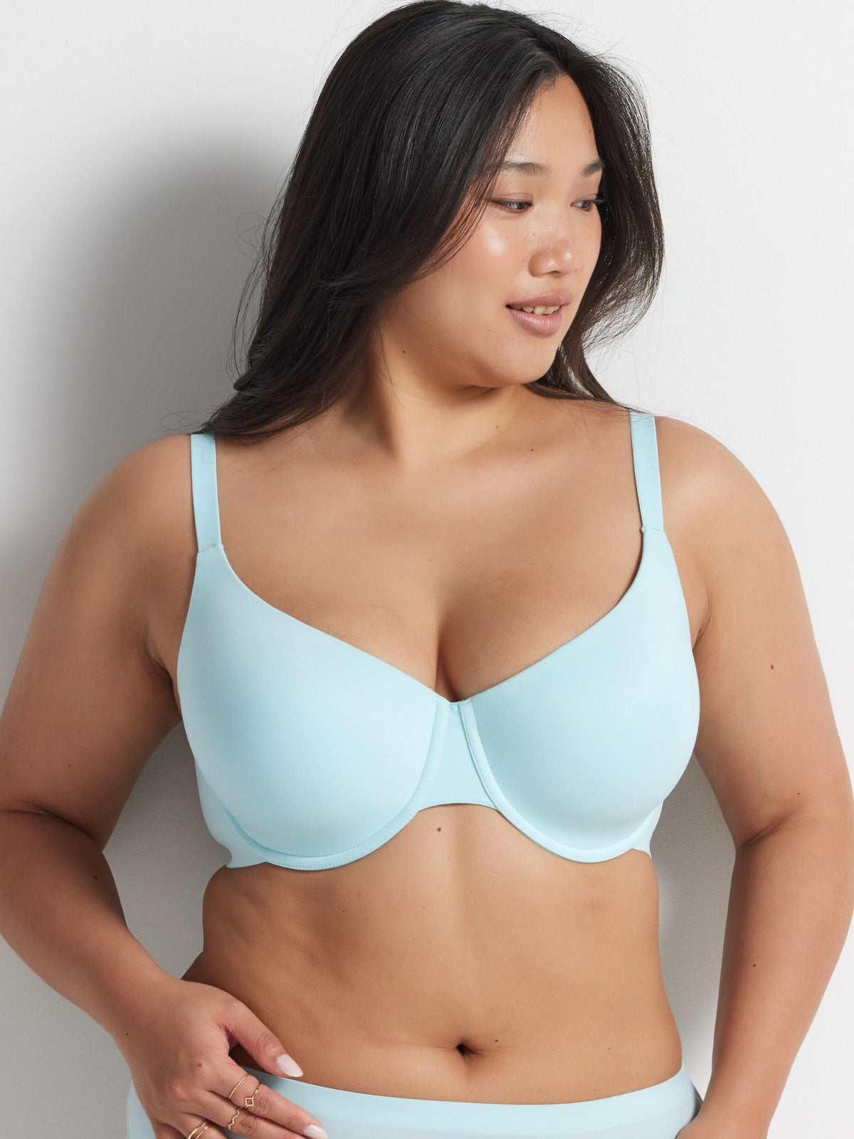 Woman wearing the aqua blue Alive T-Shirt Bra and matching briefs, standing against a grey wall.