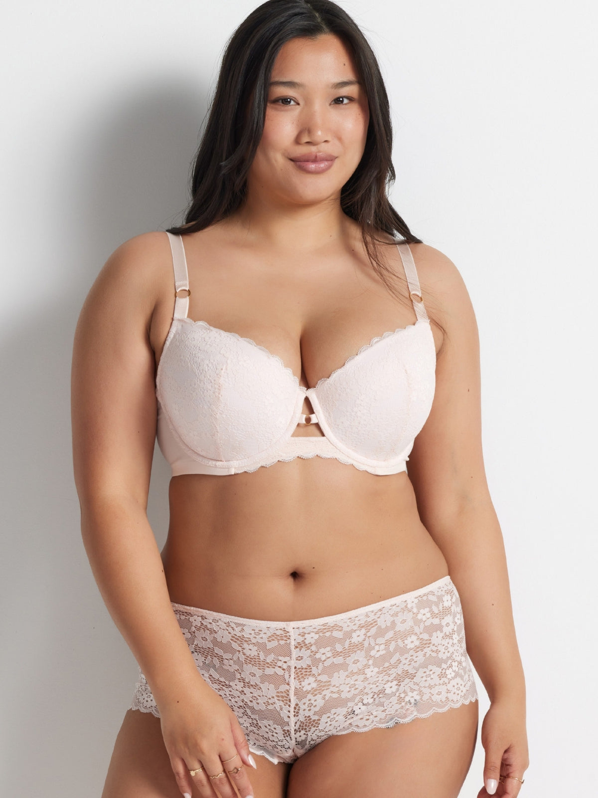 Chloe is wearing the Be Free Lace Short in Shell with matching bra, standing against a grey wall.