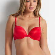 Frankie is wearing the Bombshell Super Boost Bra in Fire Engine with matching briefs, standing against a grey wall.