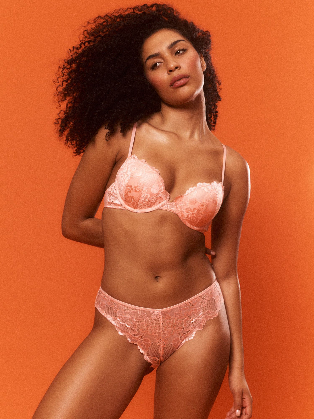 Woman wearing a pink lace lingerie set against an orange background