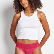 Woman wearing a white tank top and pink underwear against a plain background