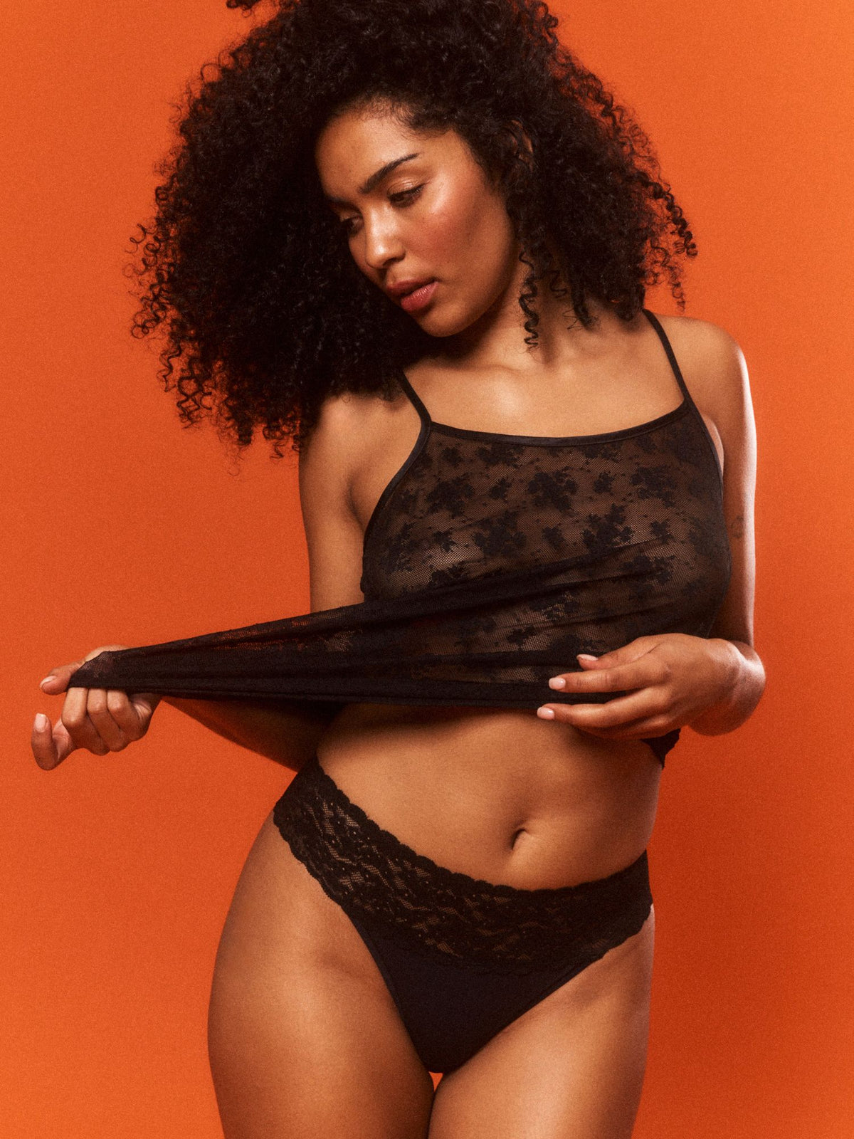 Jaida is wearing a black lace lingerie set against an orange background