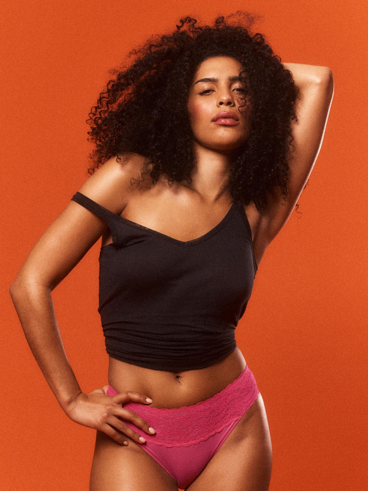 Woman wearing a black top and pink underwear against an orange background
