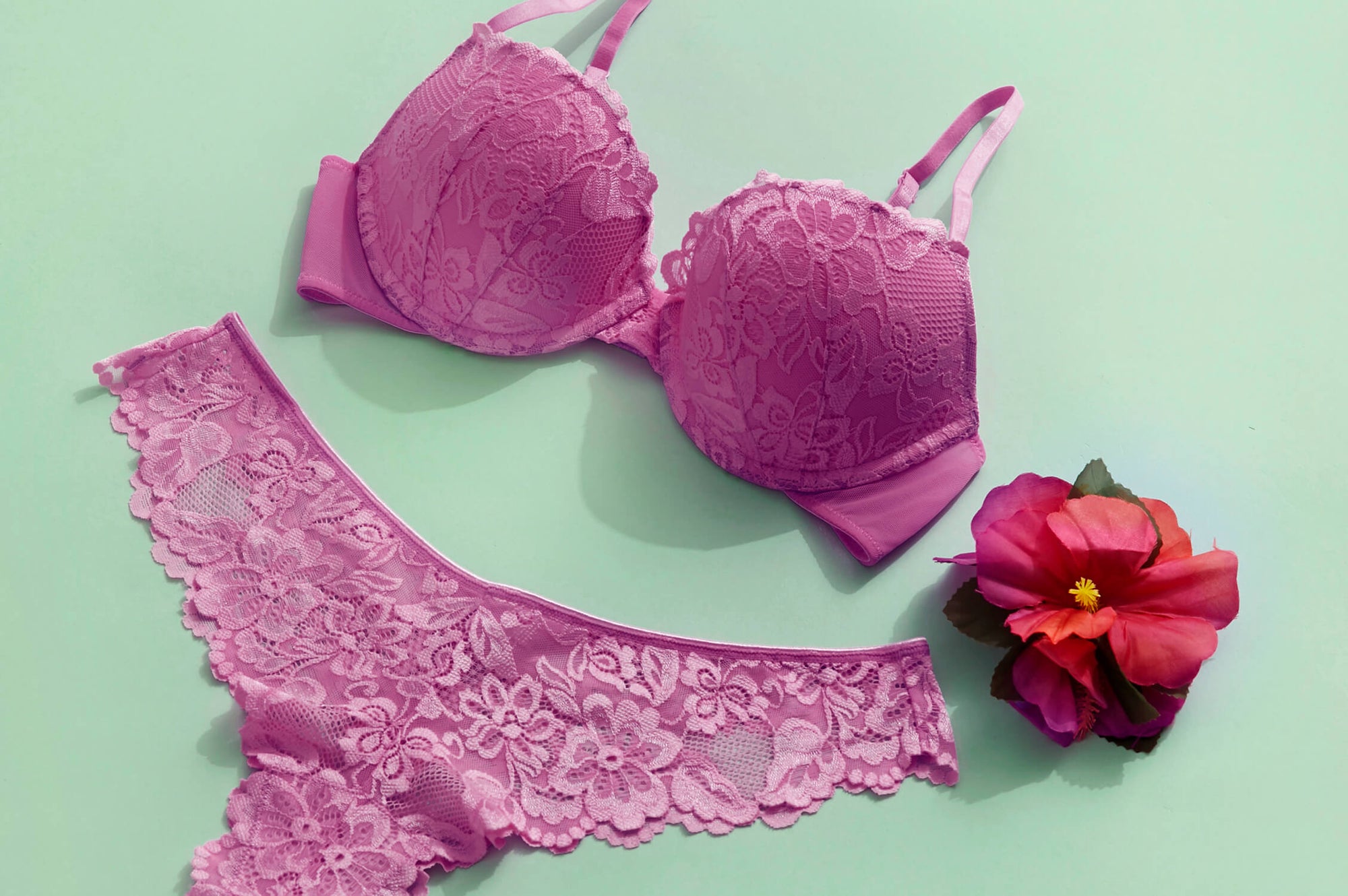 A Pink Brazilian Push Up Bra and matching Brazilian bikini on a mint green background with a pink flower