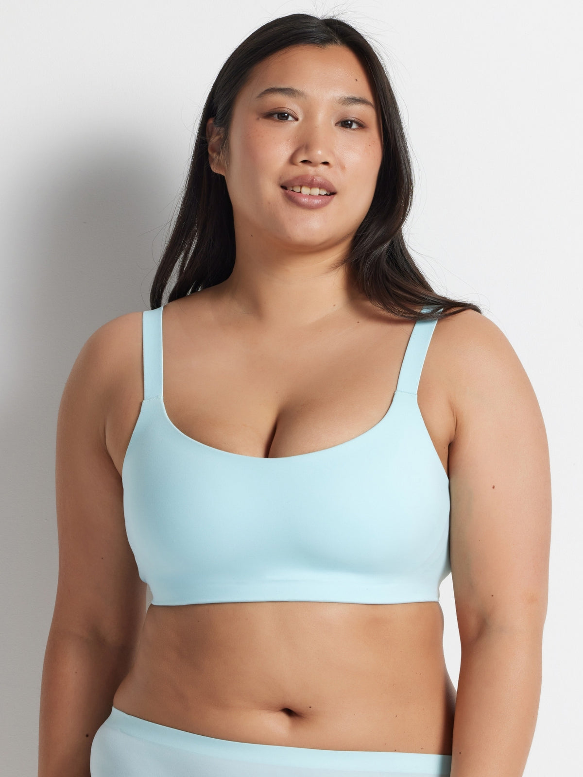 Woman wearing the aqua blue Alive Bandeau Bra with matching briefs, standing against a grey wall.