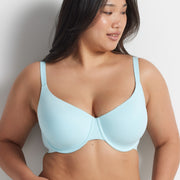 Woman wearing the aqua blue Alive T-Shirt Bra and matching briefs, standing against a grey wall.
