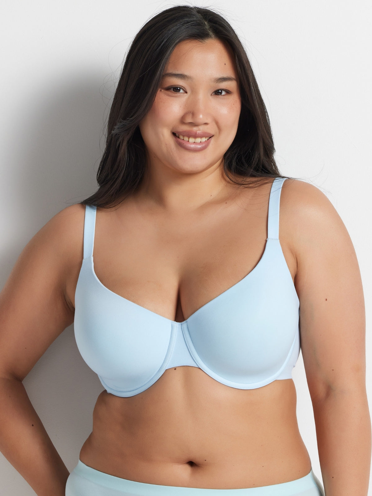 Chloe is wearing the Alive T-Shirt Bra in Blue with matching briefs, standing against a grey wall.