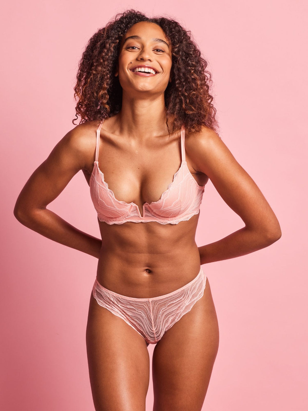 Woman wearing a pink bra and underwear set against a pink background